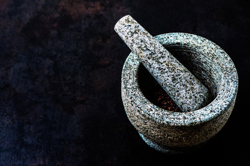 Stone mortar bowl and pestle on dark stone surface