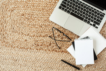 Blank sheet notebook, laptop, glasses, pen, laptop on wicker straw background. Flat lay, top view...