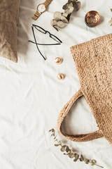 Fototapeta premium Fashion women accessories, straw bag, pillow, eucalyptus branches on white linen. Flat lay, top view fashion blogger concept for social media, website, blog.
