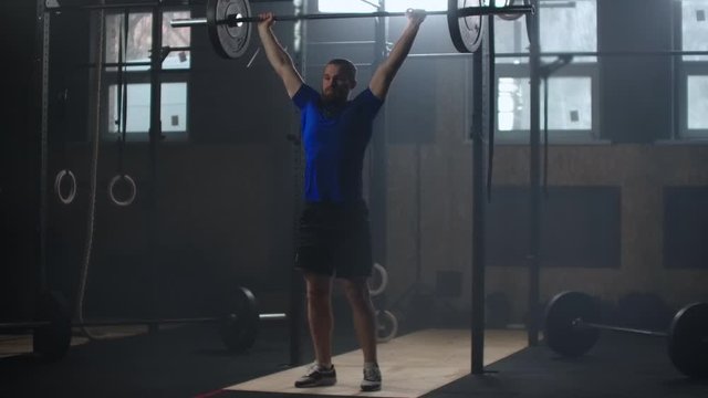 Young sportsman lifting heavy barbell. Healthy, muscular. Strong man doing barbell snatch exercise at the gym in slow motion. Sportsman on exercise mat doing situps in gym. 