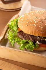 Juicy bacon burger on wooden table. Delicious fastfood grilled fresh tasty burger. Tasty grilled home made burger with beef, tomato, cheese, bacon and lettuce. Hamburger with fries and different sauce