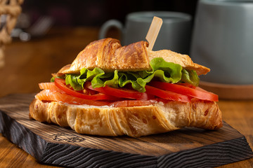 Croissant with smoked salted salmon, tomato. Croissant sandwiches served on wooden board. Croissants with egg, melted cheese, parsley, chicken ham, smoked salmon.