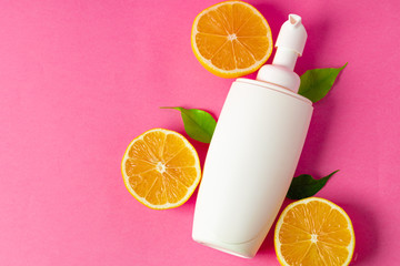 Cosmetic bottle with sliced citrus fruits on bright pink background