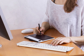 The hands of young woman, artist or graphic designer, drawing on graphic tablet and using wireless keyboard and mouse at home office. Woman freelance. Indoors, copy space.