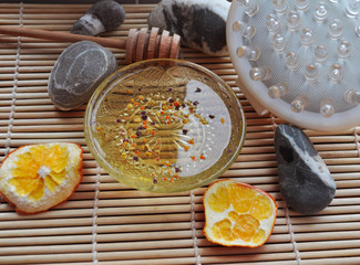 honey spa treatments with honey and massager on the background of hot stones and fragrant orange peels