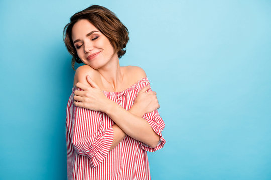 Photo of pretty lady dreamer hug herself enjoy own company eyes closed peaceful good mood wear casual white red open naked shoulders blouse isolated blue color background