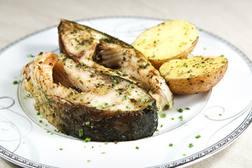 Pieces of baked carp with potatoes in plate. Dish of fish carp pieces and unpeeled potatoes baked in oven..