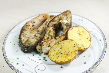 Pieces of baked carp with potatoes in plate. Dish of fish carp pieces and unpeeled potatoes baked in oven..
