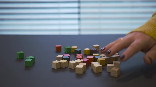 Young female hand with a red manicure in sweater mixing coloured wooden blocks with uncoloured. Closeup video where girl playing with the wooden blocks.