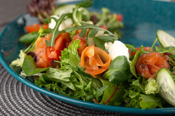 Delicious fresh salad. Salad with salmon, mozzarella cheese, cherry tomatoes, arugula, olive oil. Fresh salmon salad with mozzarella and vegetables. Close up view on Salad. Healthy, diet tasty summer 