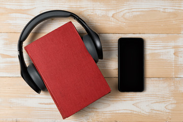Book, headphones and phone on wooden background. Audiobook concept. Top view, copy space