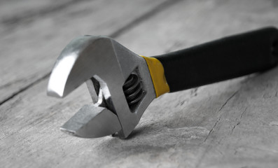 Adjustable wrench with yellow handle on the wood background
