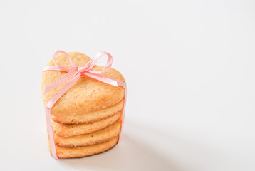 A stack of five heart-shaped sugar cookies tied with a pink ribbon with a bow. Gift treat for Valentine's day on white background with copy space.