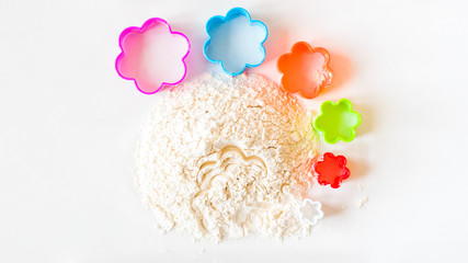 A slide of flour on a white background and a set of six bright cookie cutters in the form of a...