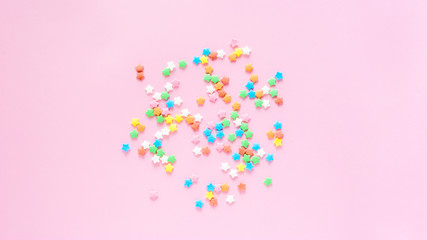Colored sugar stars sprinkled on a pastel light pink background, top view and copy space.
