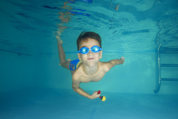 A boy in goggles plays underwater in a swimming pool