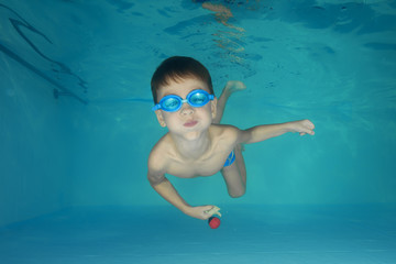 A boy in goggles plays underwater in a swimming pool