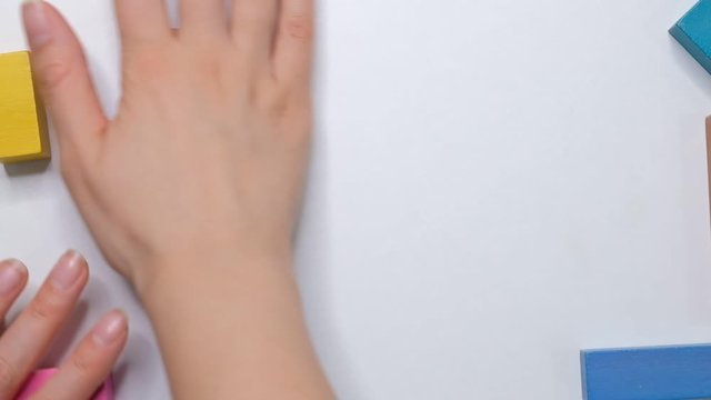 female hands clean wooden cubes from a white table, flat lay, frame children's cubes, concept of children's education