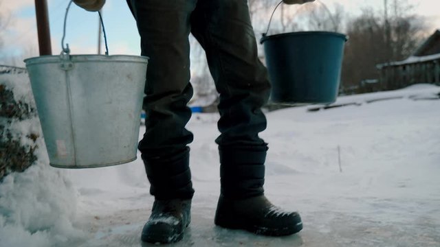 An elderly man with buckets in winter carries water from a well.