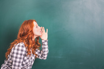 young beautiful schoolgirl with red hair stands in front of blackboard and talks