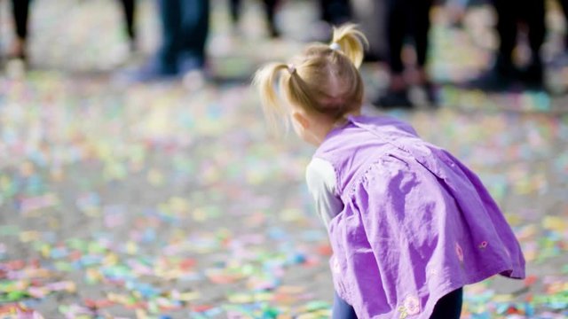 Cute girl with poneytails dressed in violet playing with confetti on cobblestone ground