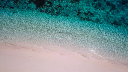 Fototapeta premium A drone shot of a pink sand beach on a small island near Maumere, Indonesia. Happy and careless moments. Waves gently washing the shore.Clear, turquoise coloured water displaying coral reef.