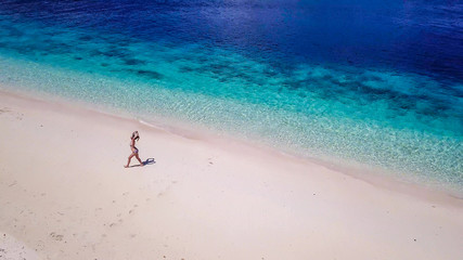 Fototapeta na wymiar A drone shot of a girl playing on the beach on a small island near Maumere, Indonesia. Happy and careless moments. The coast changes colors from white to turquoise and navy blue. There are few islands