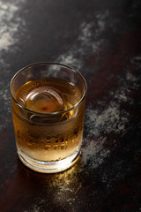 glass with strong whiskey and ice cube on black surface
