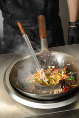 Man Chef cooking food in restuarant. Cook prepares asian food in wok. man cooks rice with vegetables in a wok. Close up process of cooking rice with vegetables.