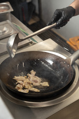 Cooking in the kitchen in a wok with smoke and boiling oil. Man Chef cooking food in restuarant. Cook prepares asian food in wok. man cooks chicken in a wok. Close up process of cooking Asian food.