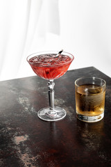 glass of whiskey near cosmopolitan cocktail with ice cubes on white