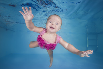 Fototapeta na wymiar little girl in a pink swimsuit learns to dive underwater in the swimming pool
