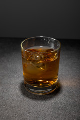 frozen ice cubes in glass of whiskey on grey surface