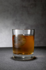 frozen ice cube in glass of whiskey on grey