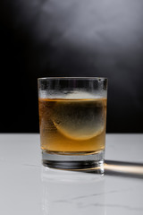 ice cube in glass of whiskey on black with smoke