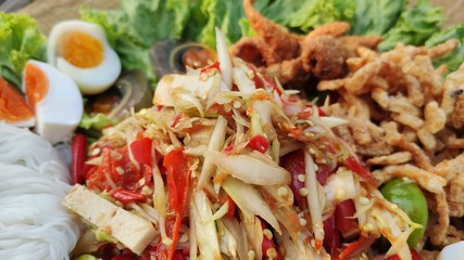 Papaya salad, boiled eggs, fried chicken skin, rice noodles, pork sausage, vegetables background lunch