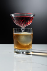 selective focus of ice cube in glass of whiskey near red wine on black