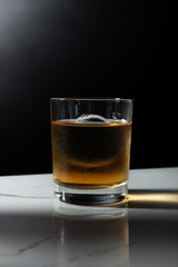 ice cube in glass of strong whiskey isolated on black