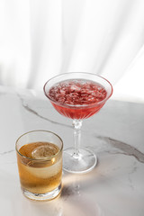 glass of strong brandy near red cocktail with ice cubes on white