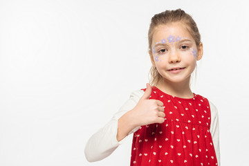 adorable child with floral painting on face smiling at camera and showing thumb up isolated on white