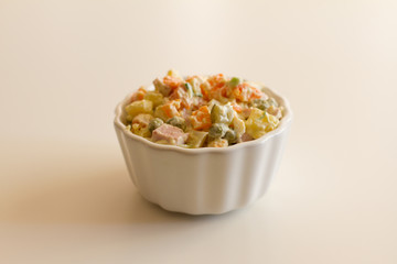 Olivier in a white plate on a pale pink background. the winter salad.ingredients: cucumber, sausage, meat, mayonnaise, sour cream, potatoes, peas, egg. space for your text.