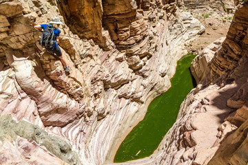 Young woman climbing down in a canyon with a natural pool at the bottom and steep rock faces around...