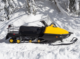 Side view of yellow snowmobile on snow at winter sunny day