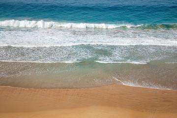 Aerial view of a golden yellow beach where waves crushes, produce white foam  with colorful water blue turquoise azure aquamarine