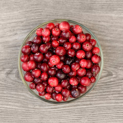 The fresh unpeeled cranberry in the glass bowl on the wooden texture, the top view.