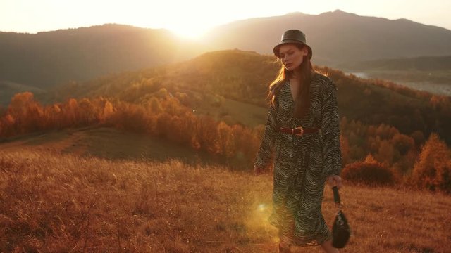 Outdoor autumn fashion portrait of young beautiful confident woman posing at sunset in mountain landscape.