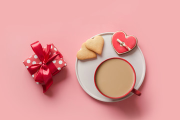 Cup of coffee, gift and biscuits in shape of heart on pink light background. Valentine cookies with love letter. Flat lay, copy space