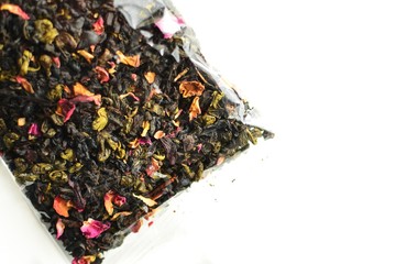 Black tea in a plastic transparent bag. Tea with flowers and packaging on a white background isolated. View from above.