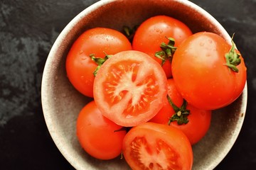 Ripe tomatoes in a gray clay bowl. Whole Tomatoes close-up on a concrete dark table background. Healthy raw vegetables.