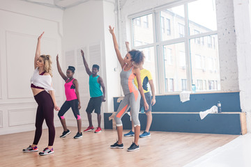 Trainer and multiethnic dancers with hands in air practicing zumba in dance studio
